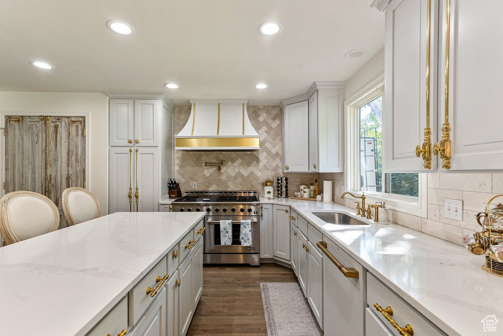 Kitchen with white cabinetry, range with two ovens, light stone counters, and premium range hood
