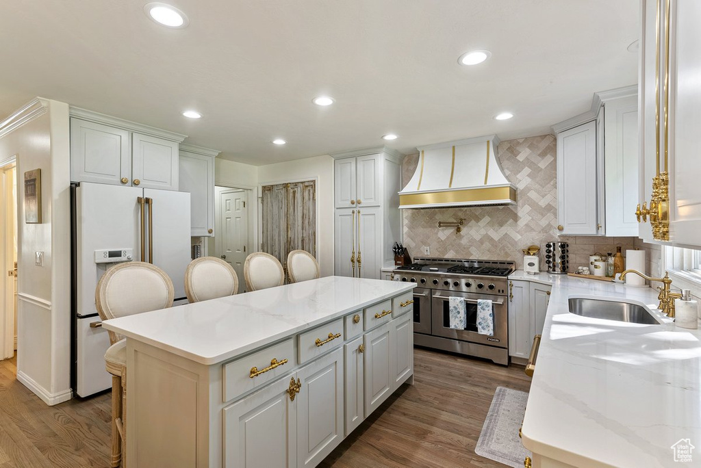 Kitchen featuring light stone counters, a breakfast bar, custom range hood, high quality appliances, and white cabinetry
