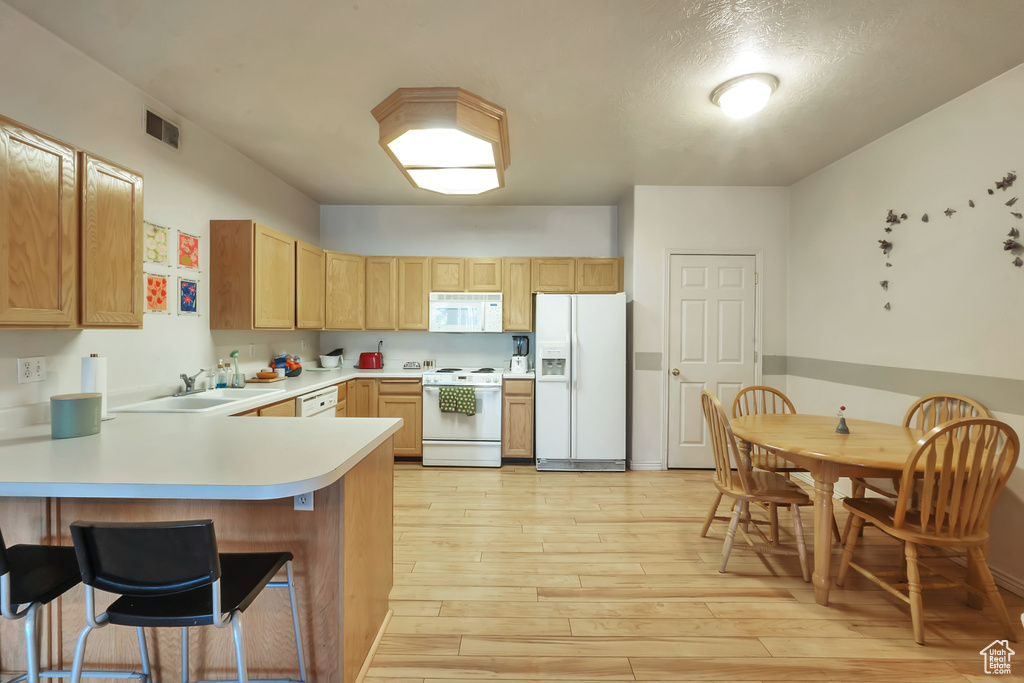 Kitchen featuring light hardwood / wood-style floors, a kitchen bar, kitchen peninsula, white appliances, and sink