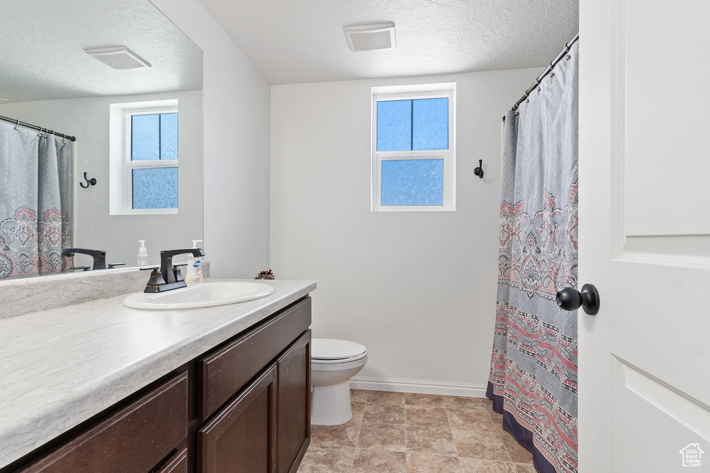 Bathroom featuring tile flooring, a textured ceiling, oversized vanity, and toilet