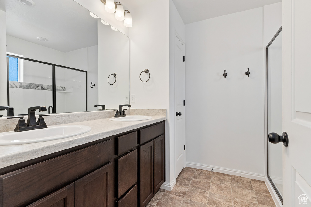 Bathroom featuring a shower with shower door, dual sinks, vanity with extensive cabinet space, and tile flooring