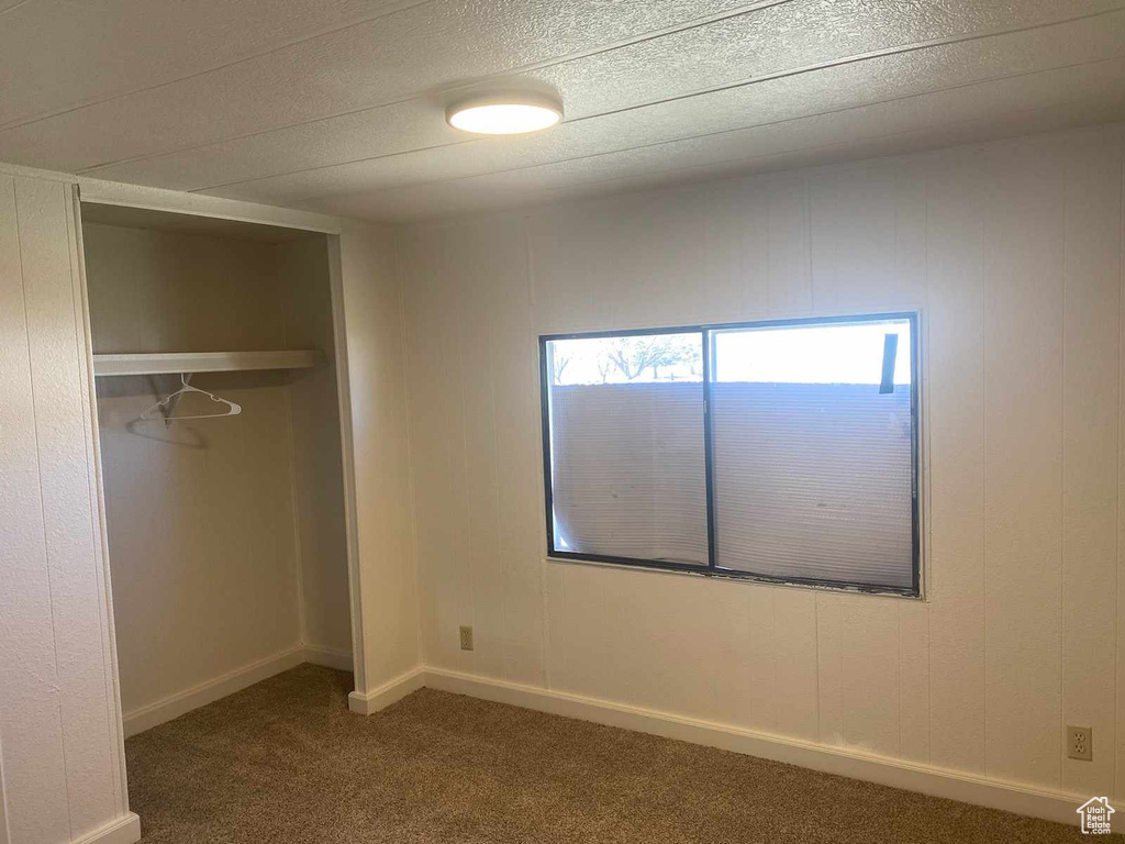 Unfurnished bedroom with a textured ceiling, dark carpet, and a closet