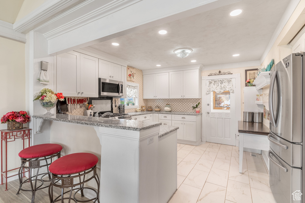 Kitchen featuring backsplash, stainless steel appliances, white cabinetry, and light stone counters
