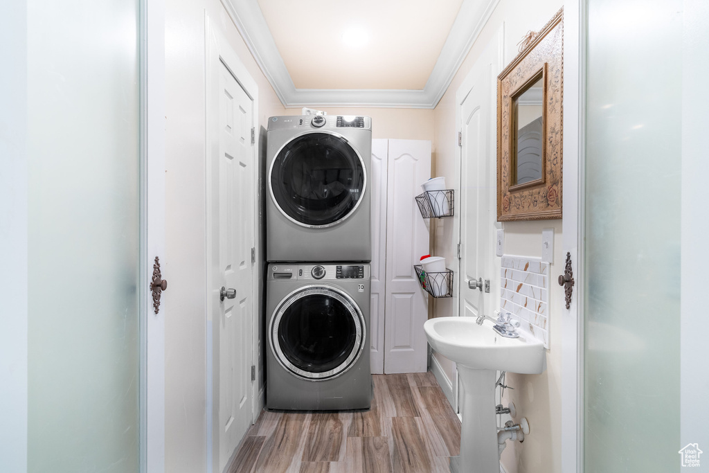 Washroom featuring stacked washing maching and dryer, light hardwood / wood-style floors, and ornamental molding