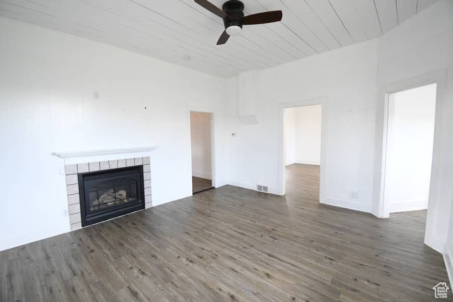 Unfurnished living room with dark hardwood / wood-style flooring, ceiling fan, and a tile fireplace