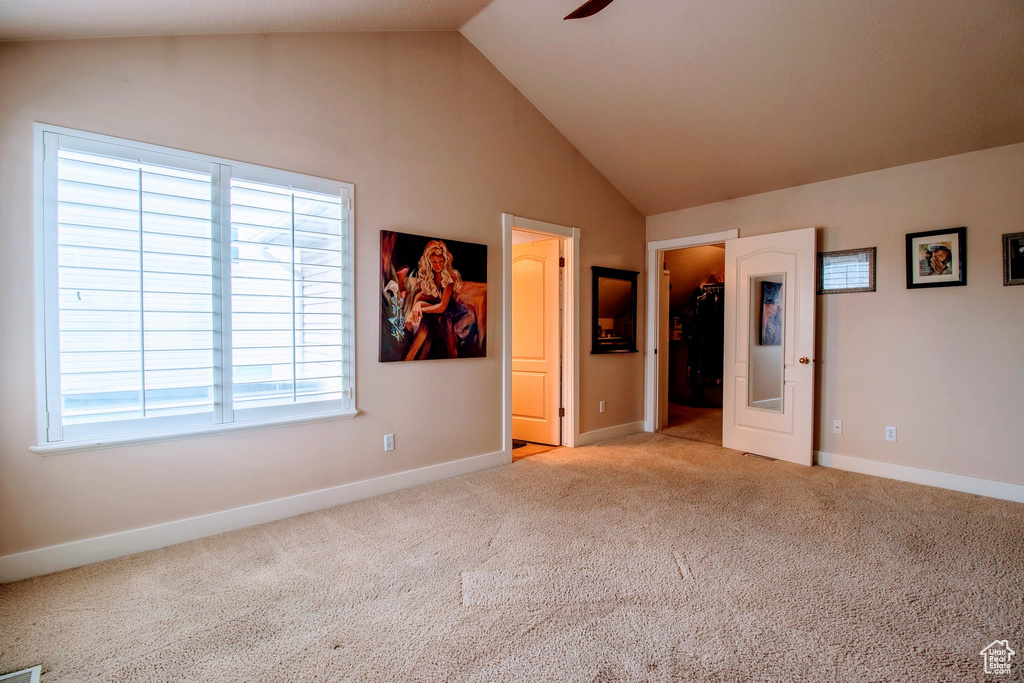 Unfurnished bedroom with light carpet, a walk in closet, and high vaulted ceiling