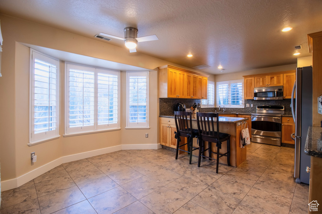 Kitchen featuring a kitchen breakfast bar, backsplash, stainless steel appliances, light tile floors, and ceiling fan
