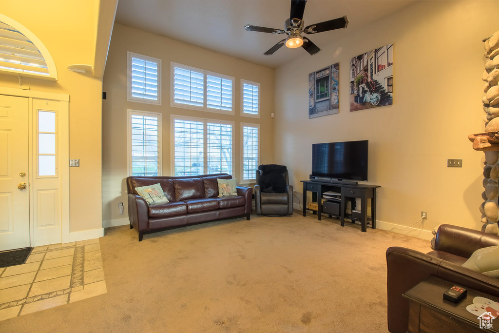 Living room featuring ceiling fan, light carpet, and a towering ceiling
