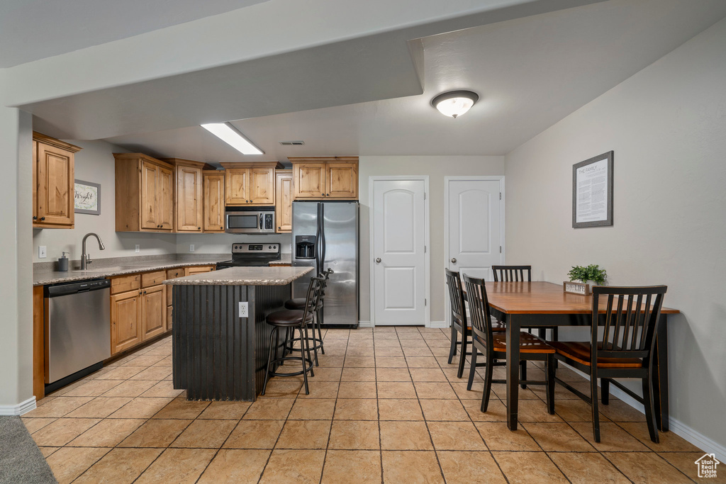 Kitchen with light tile flooring, a breakfast bar area, a center island, and appliances with stainless steel finishes