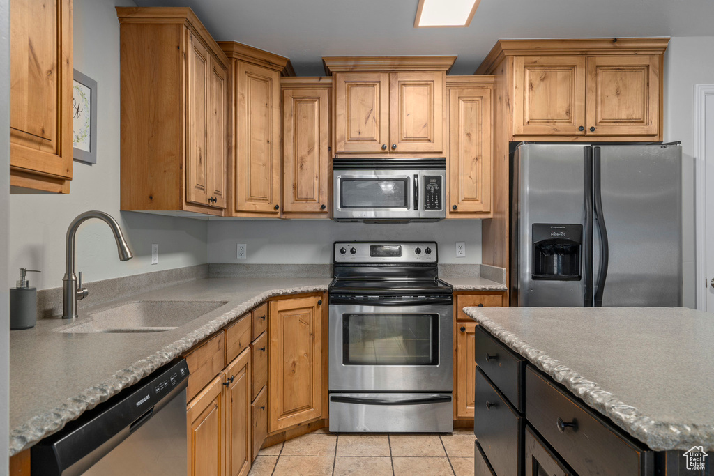 Kitchen featuring light tile floors, appliances with stainless steel finishes, light stone countertops, and sink