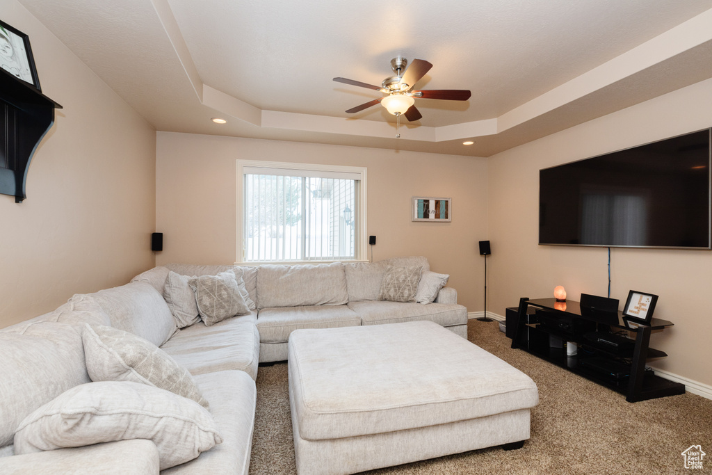 Carpeted living room with ceiling fan and a tray ceiling