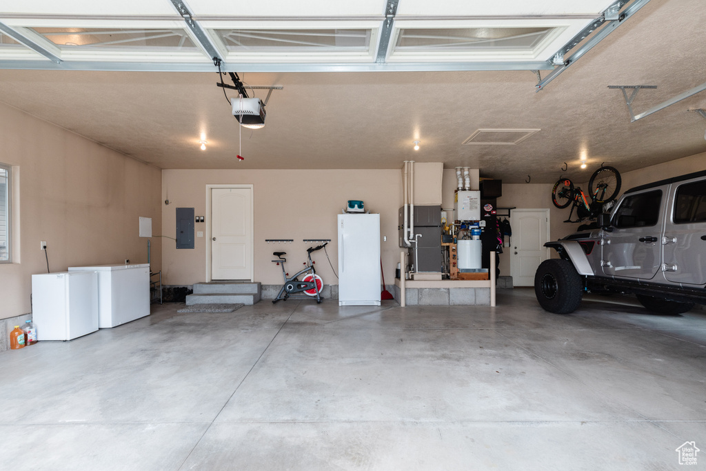 Garage featuring a garage door opener, fridge, and white fridge