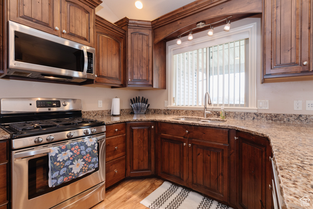 Kitchen with light wood-type flooring, light stone countertops, appliances with stainless steel finishes, and sink