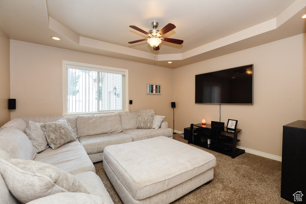 Carpeted living room with a tray ceiling and ceiling fan