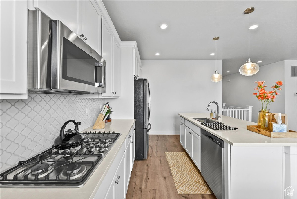 Kitchen featuring decorative light fixtures, tasteful backsplash, appliances with stainless steel finishes, white cabinets, and light wood-type flooring
