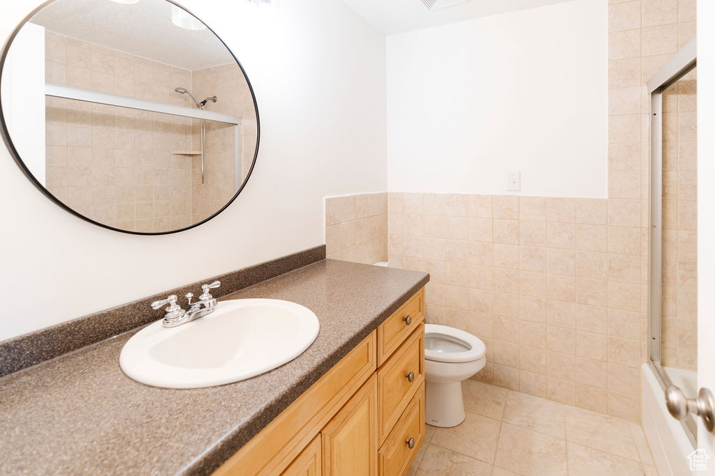 Full bathroom featuring tile walls, oversized vanity, tile flooring, combined bath / shower with glass door, and toilet