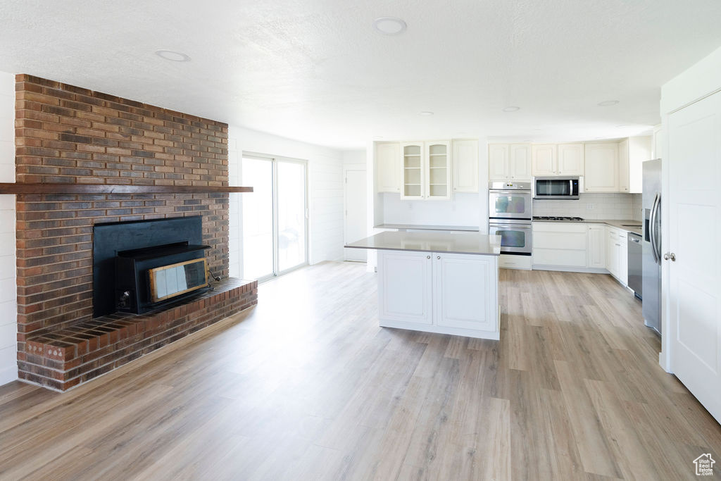 Kitchen with a center island, white cabinets, a brick fireplace, appliances with stainless steel finishes, and light hardwood / wood-style floors
