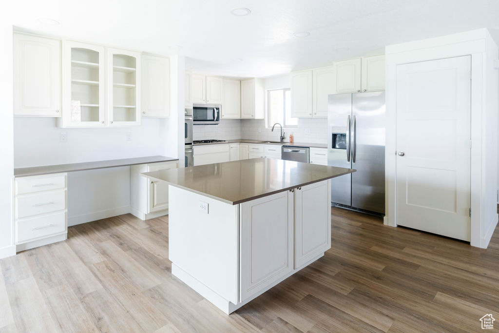 Kitchen featuring appliances with stainless steel finishes, a center island, sink, white cabinetry, and light hardwood / wood-style flooring