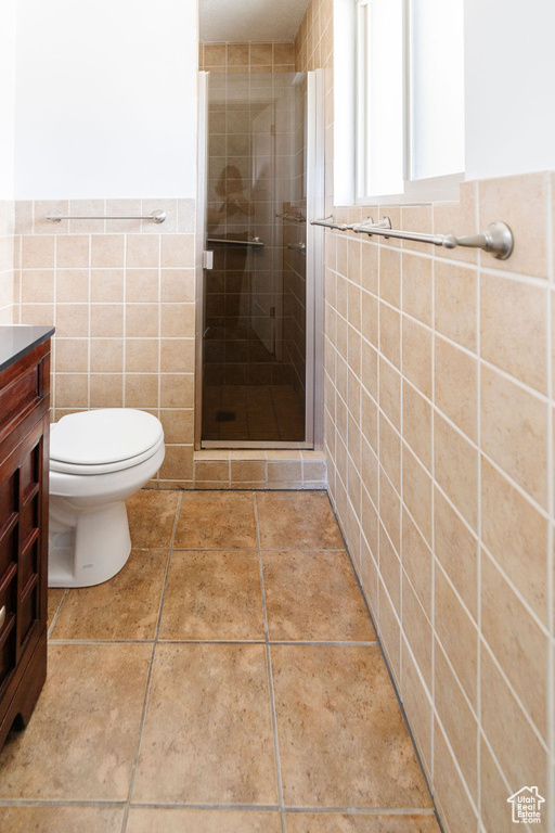 Bathroom featuring tile walls, an enclosed shower, tile floors, toilet, and vanity