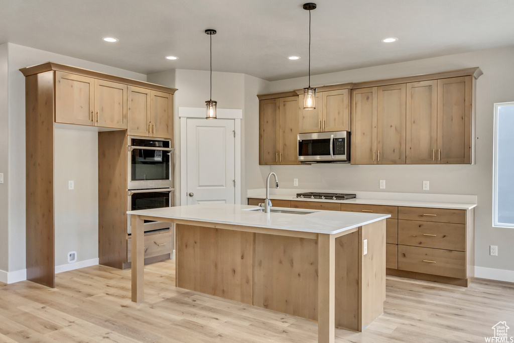 Kitchen with a kitchen island with sink, pendant lighting, sink, appliances with stainless steel finishes, and light wood-type flooring