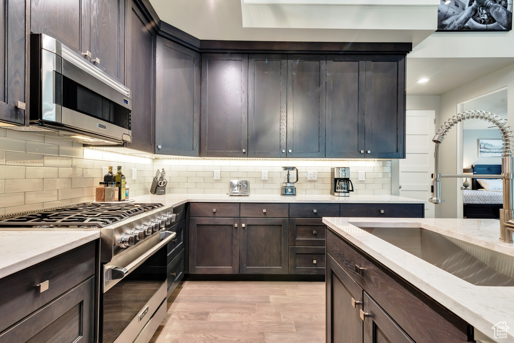 Kitchen featuring appliances with stainless steel finishes, backsplash, light wood-type flooring, and dark brown cabinetry