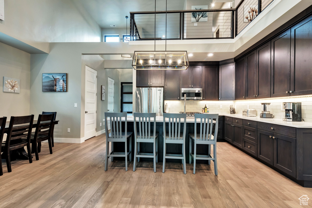 Kitchen featuring decorative light fixtures, light hardwood / wood-style flooring, appliances with stainless steel finishes, and a towering ceiling