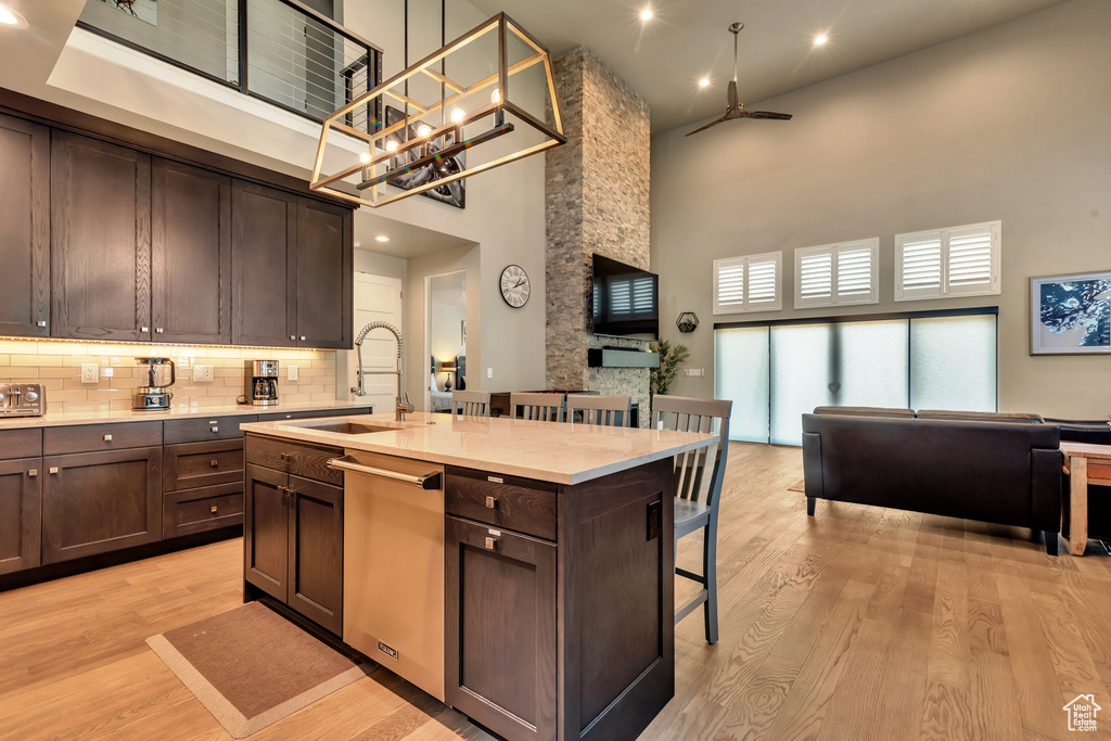 Kitchen featuring dark brown cabinetry, light hardwood / wood-style floors, a kitchen island with sink, dishwasher, and a high ceiling