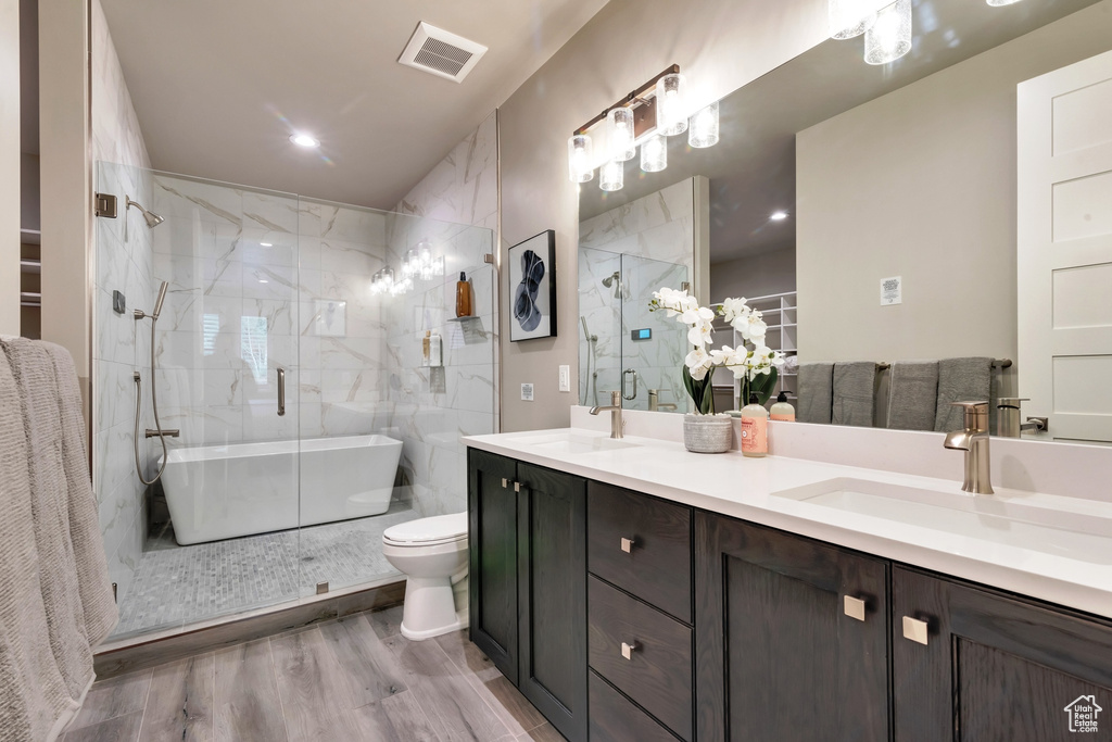 Bathroom with dual sinks, hardwood / wood-style flooring, toilet, a shower with shower door, and vanity with extensive cabinet space