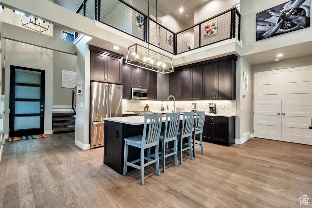 Kitchen with tasteful backsplash, light hardwood / wood-style floors, a high ceiling, and appliances with stainless steel finishes