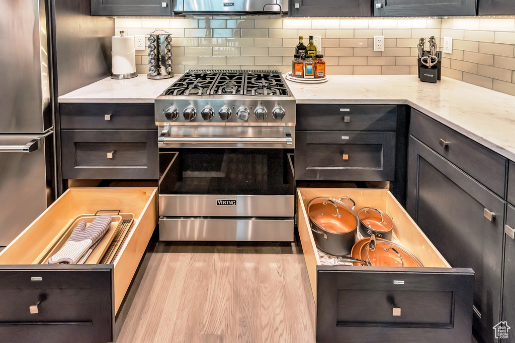 Kitchen featuring light wood-type flooring, light stone countertops, stainless steel appliances, and backsplash