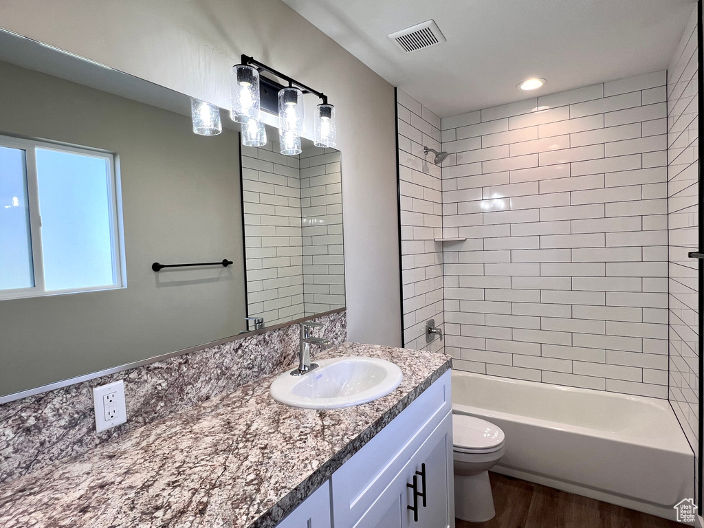 Full bathroom featuring tiled shower / bath combo, vanity, toilet, and hardwood / wood-style flooring