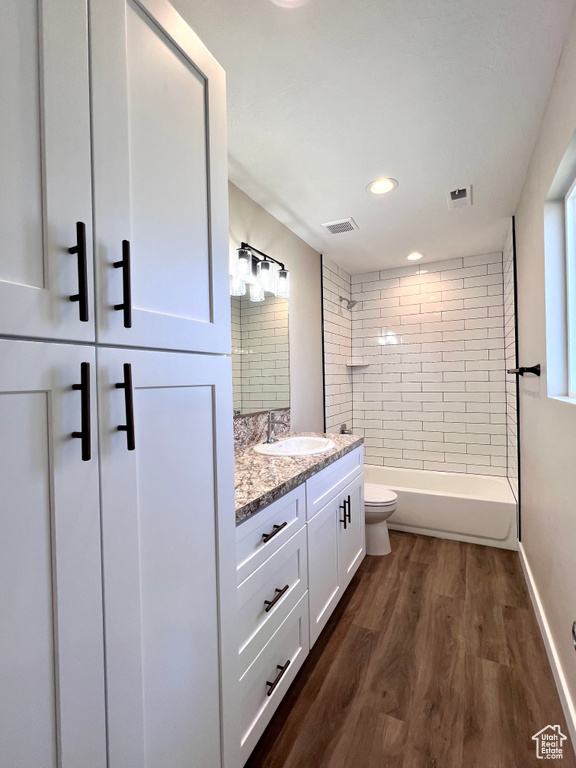 Full bathroom with toilet, tiled shower / bath combo, vanity, and wood-type flooring