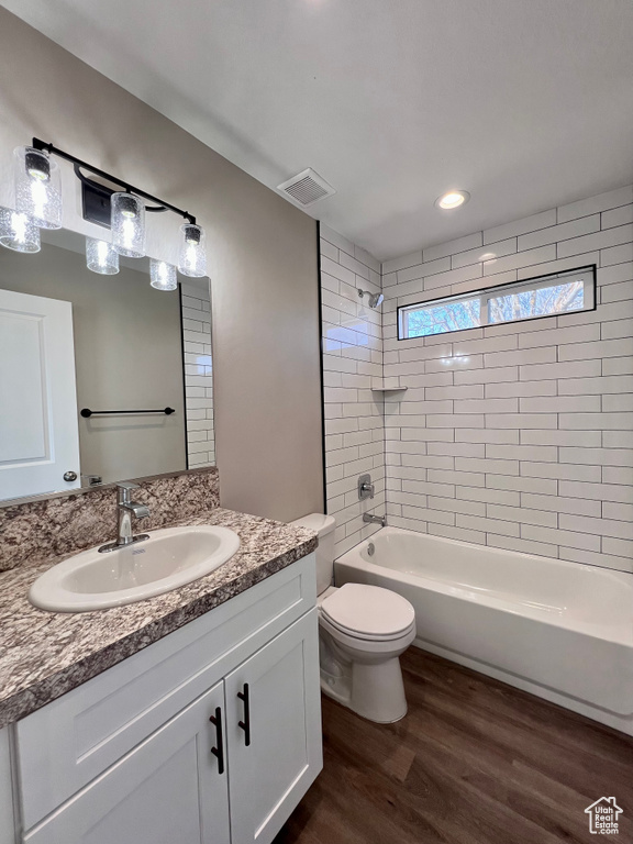 Full bathroom with oversized vanity, tiled shower / bath combo, toilet, and hardwood / wood-style flooring
