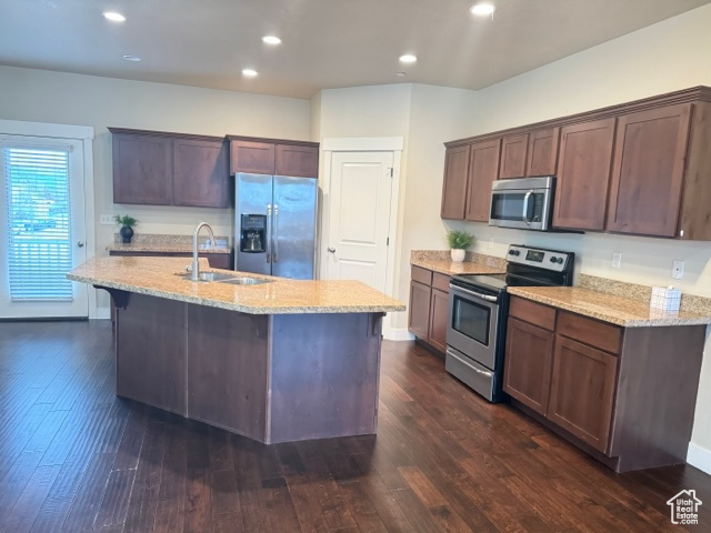 Kitchen with appliances with stainless steel finishes, dark brown cabinets, dark hardwood / wood-style flooring, and an island with sink