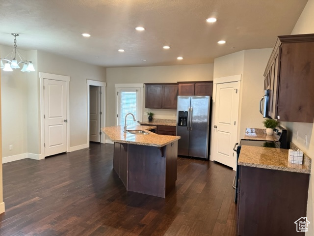 Kitchen with an inviting chandelier, stainless steel appliances, an island with sink, dark hardwood / wood-style floors, and hanging light fixtures