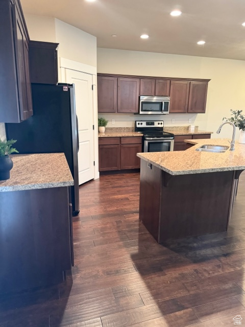 Kitchen featuring dark wood-type flooring, appliances with stainless steel finishes, dark brown cabinetry, light stone counters, and sink