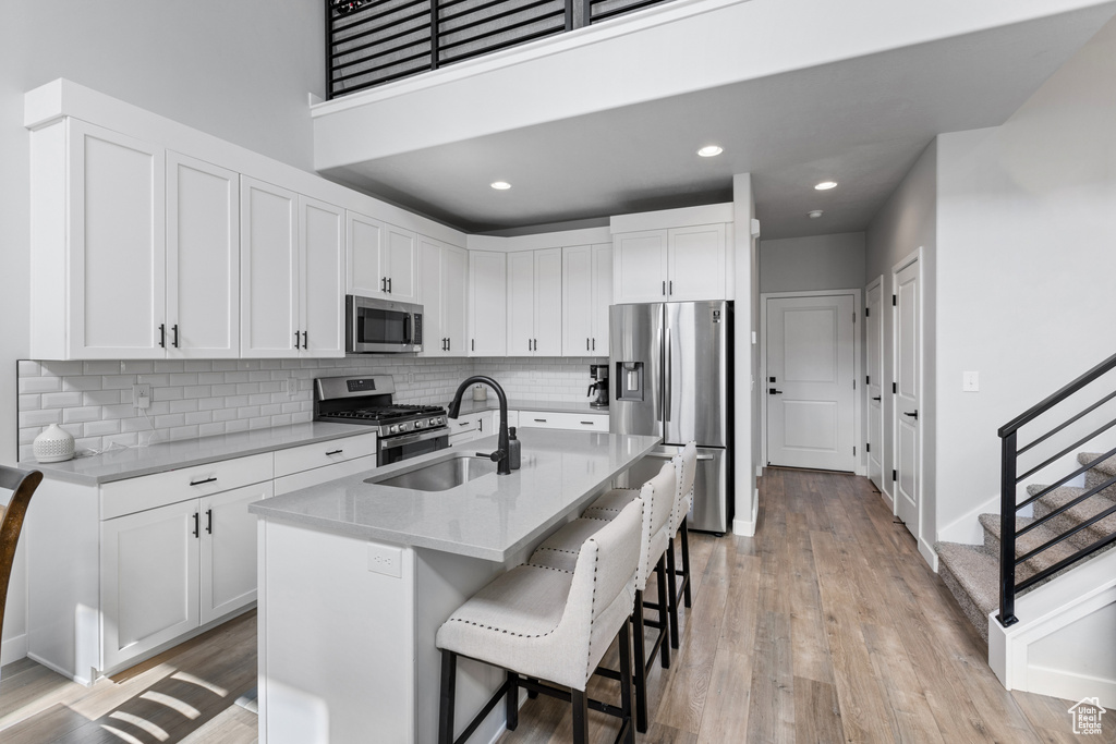 Kitchen with white cabinets, a breakfast bar area, light hardwood / wood-style floors, stainless steel appliances, and a center island with sink