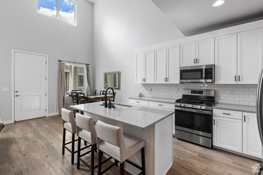 Kitchen featuring appliances with stainless steel finishes, light hardwood / wood-style floors, white cabinets, sink, and a high ceiling