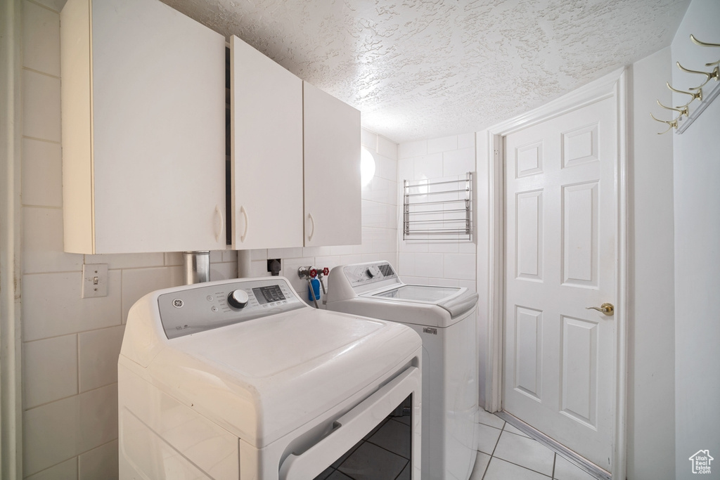 Clothes washing area with light tile flooring, a textured ceiling, cabinets, separate washer and dryer, and washer hookup