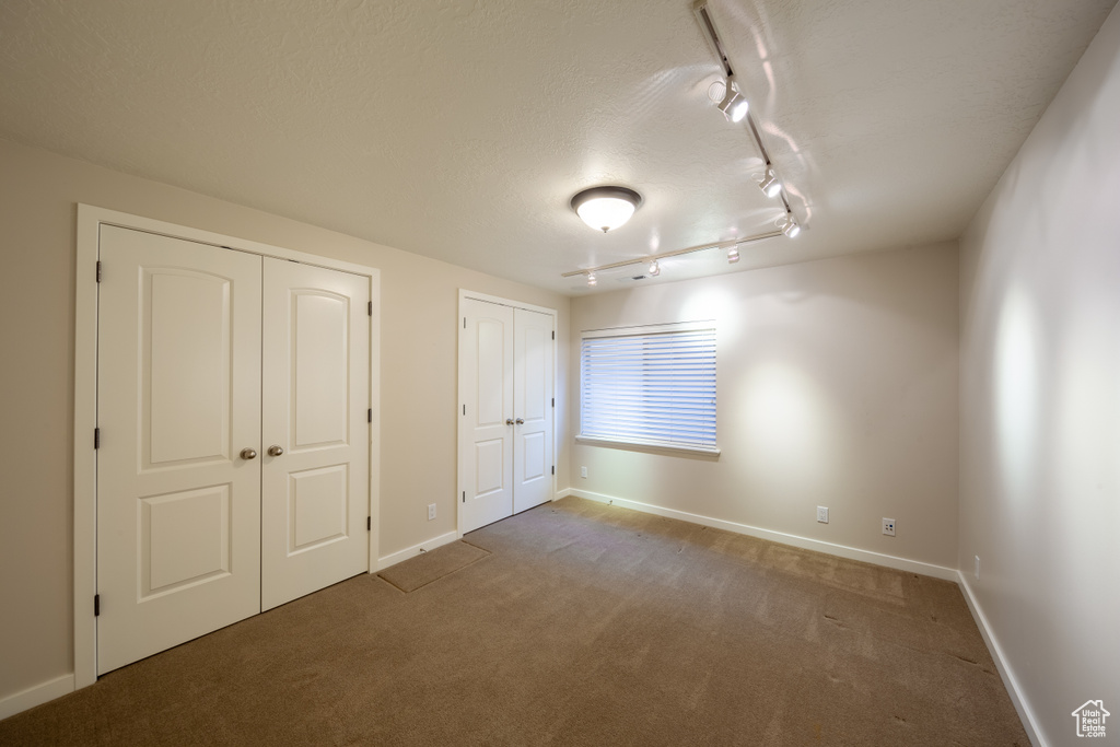 Unfurnished bedroom featuring multiple closets, dark colored carpet, and track lighting