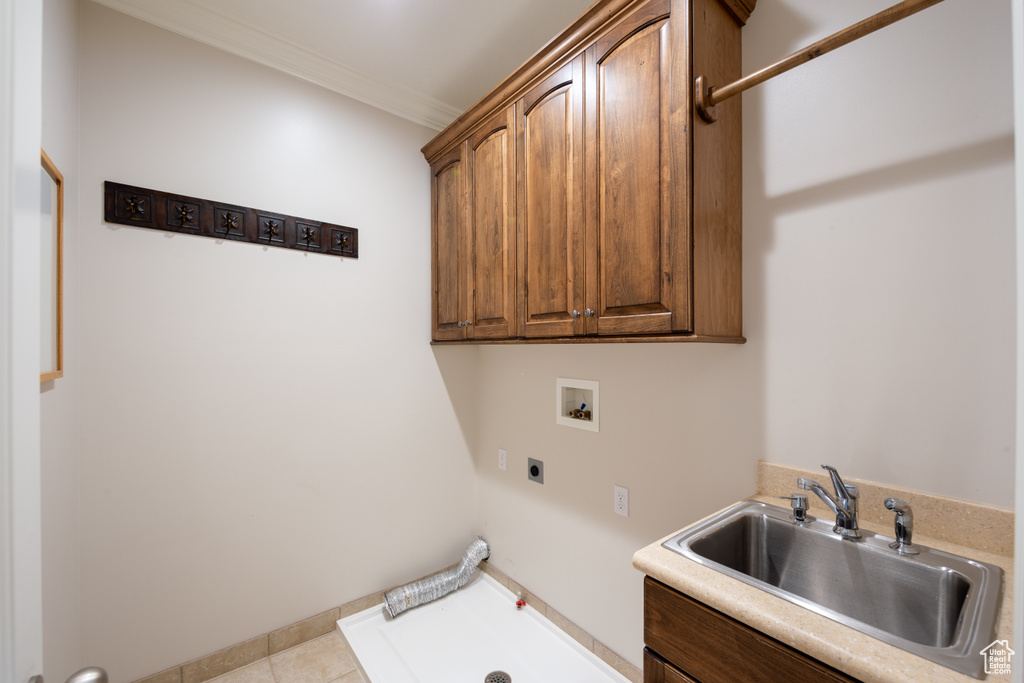 Clothes washing area with light tile flooring, gas dryer hookup, cabinets, crown molding, and sink