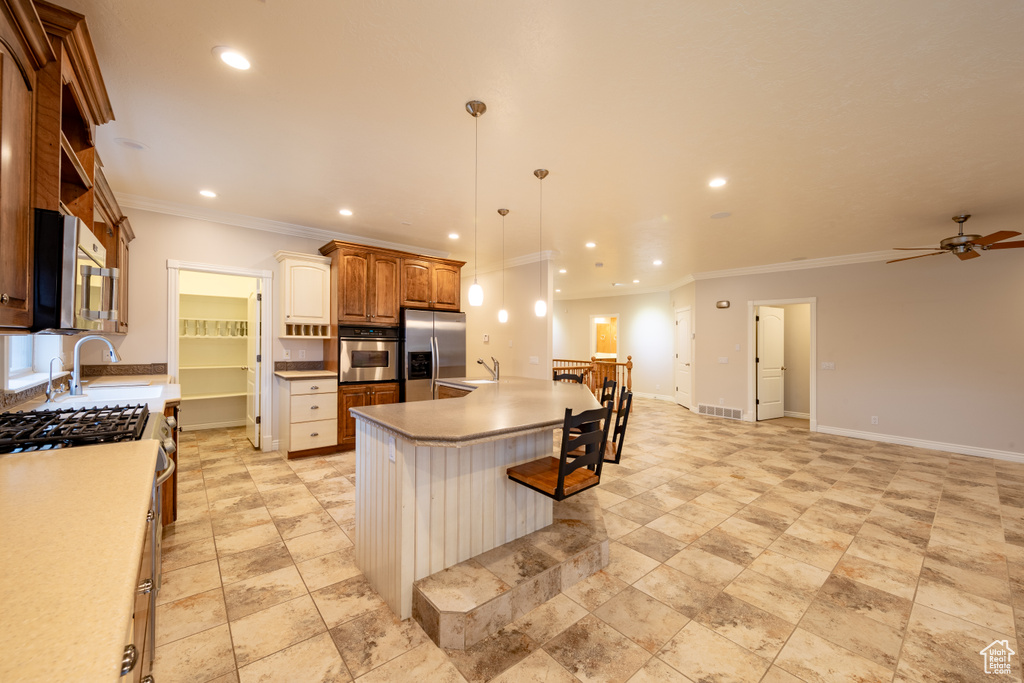 Kitchen with decorative light fixtures, ceiling fan, appliances with stainless steel finishes, an island with sink, and light tile floors