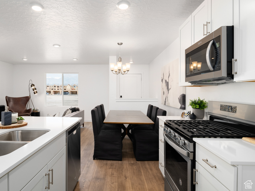 Kitchen featuring decorative light fixtures, appliances with stainless steel finishes, light hardwood / wood-style floors, white cabinets, and a chandelier