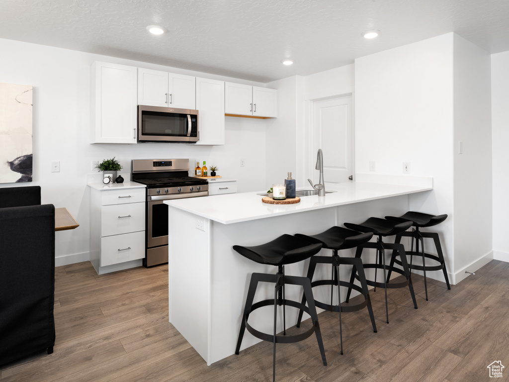 Kitchen featuring sink, white cabinets, a breakfast bar area, light hardwood / wood-style floors, and stainless steel appliances