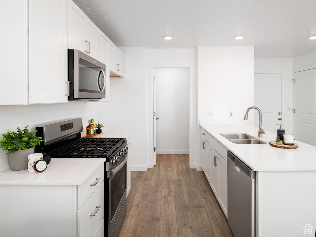 Kitchen featuring hardwood / wood-style floors, stainless steel appliances, white cabinetry, and sink