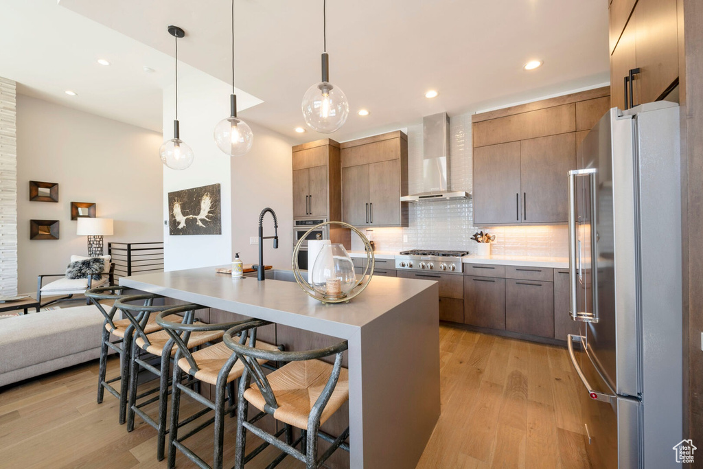 Kitchen featuring wall chimney range hood, tasteful backsplash, appliances with stainless steel finishes, and light hardwood / wood-style flooring