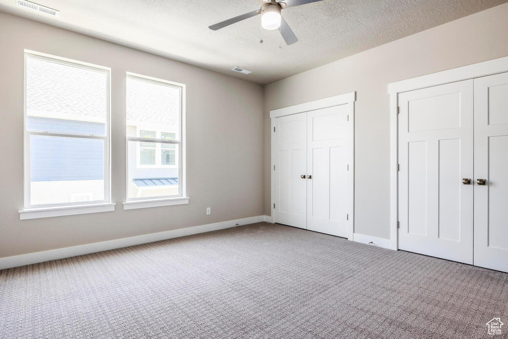 Unfurnished bedroom featuring multiple closets, ceiling fan, a textured ceiling, and light carpet