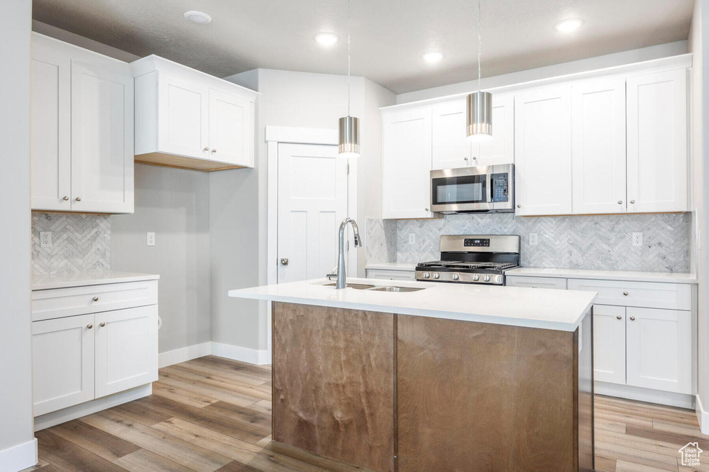 Kitchen with white cabinets, hanging light fixtures, stainless steel appliances, and light wood-type flooring