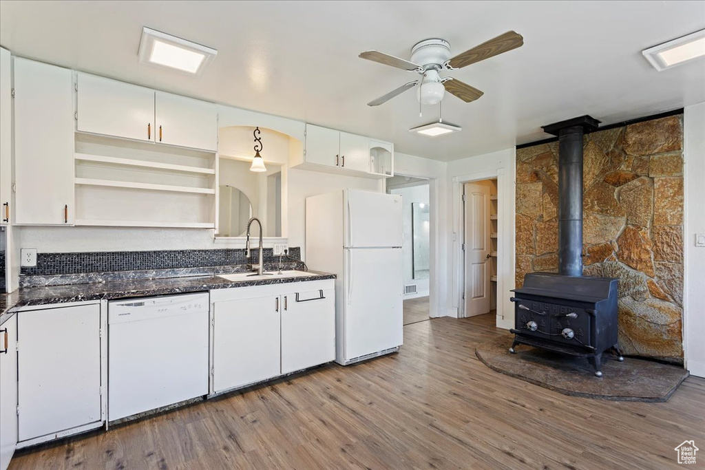 Kitchen featuring white appliances, light hardwood / wood-style floors, ceiling fan, and a wood stove