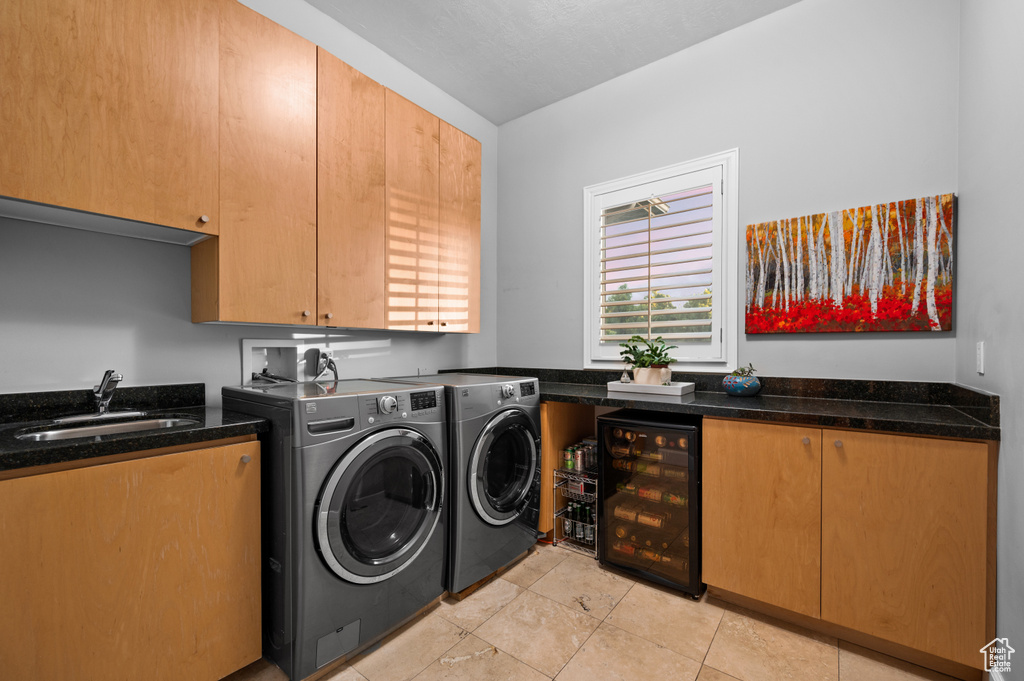Washroom featuring beverage cooler, washing machine and clothes dryer, light tile floors, sink, and cabinets